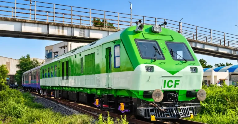 Green Indian railway power car and passenger coaches travelling beneath a railway footbridge