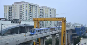 Chennai Metro Phase II train travelling along an elevated viaduct on the Porur–Vadapalani corridor, with adjoining infrastructure under construction.
