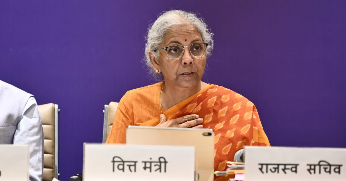 Finance Minister seated at a government meeting, wearing an orange saree, with official nameplates visible, accompanying coverage of GST Council reforms.