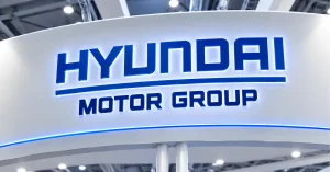 Illuminated Hyundai Motor Group logo displayed in blue lettering on a curved white corporate exhibition backdrop.