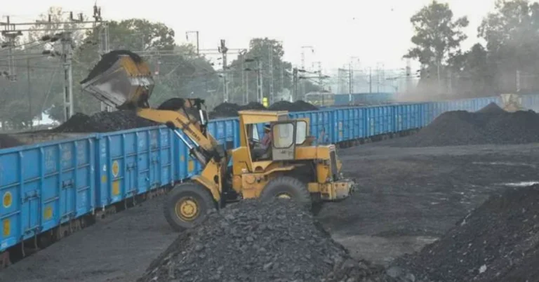 Coal loading operations at an Indian Railways siding, with a yellow wheel loader transferring coal into blue open-top freight wagons.