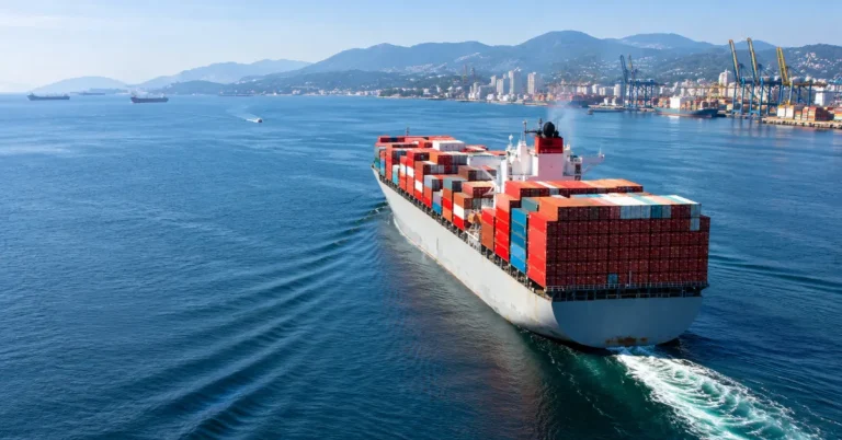 The Infra Post - India's Leading Infrastructure News Platform 22 A large container ship sailing through coastal waters with port cranes and mountains in the background, representing maritime dispute rulings under India's new shipping rules.