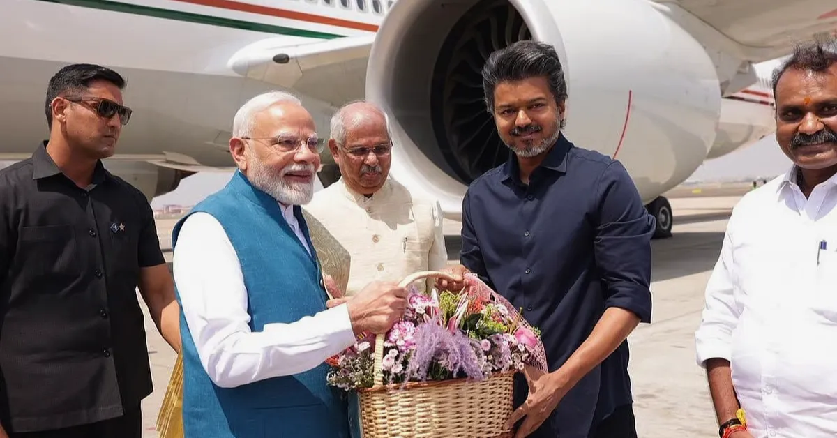Narendra Modi and C Joseph Vijay holding a floral welcome basket beside an aircraft at Chennai airport.