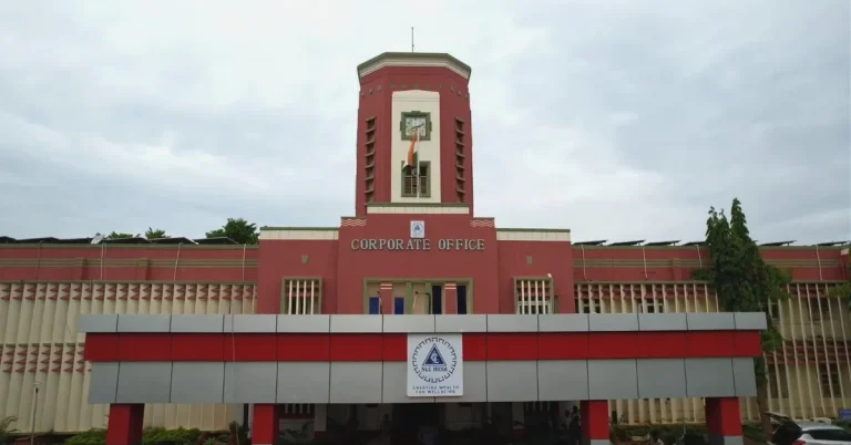 NLC India Limited corporate office building featuring a red-and-cream facade, central clock tower, Indian national flag and company emblem above the entrance.