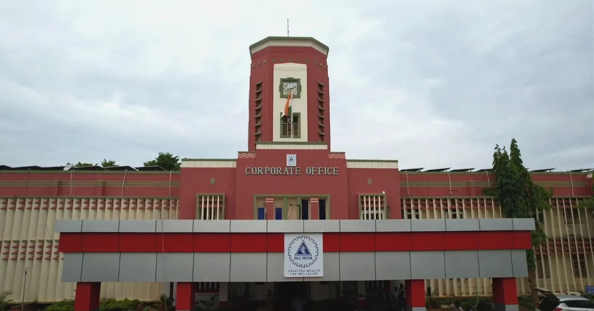 NLC India Limited corporate office building featuring a red-and-cream facade, central clock tower, Indian national flag and company emblem above the entrance.